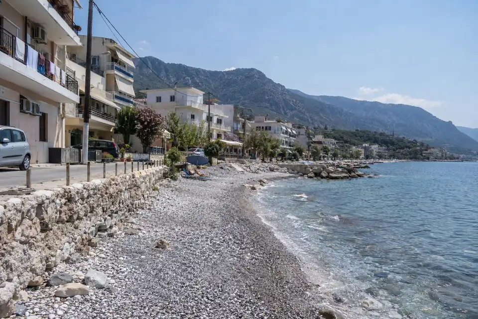 Een strand van grijze en witte kiezels, een rij vakantiehotels langs de kustweg, lage appartementenblokken met was aan de balkons.