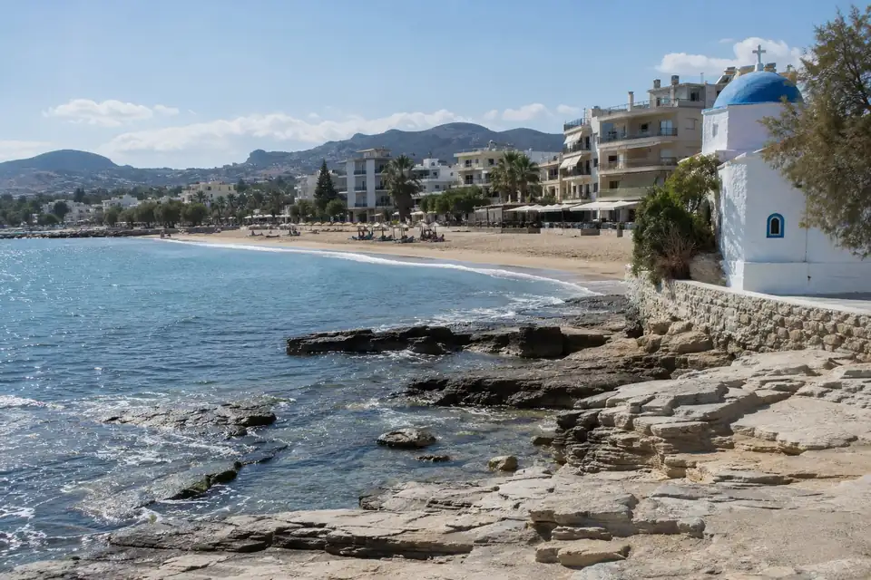 Een breed zandstrand, een rotskust van vlakke lichte platen, een rij vakantiehotels langs de kustweg.
