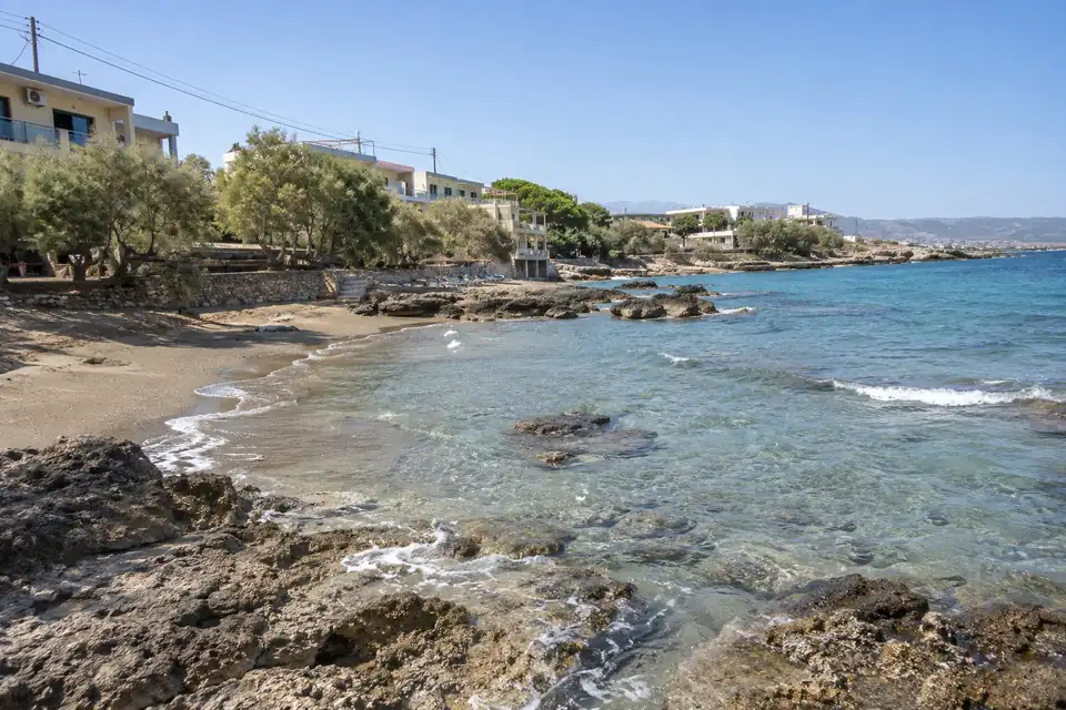 Een beschutte baai, een rij vakantiehotels langs de kustweg, een dorpsplein met plataan en cafétafels.