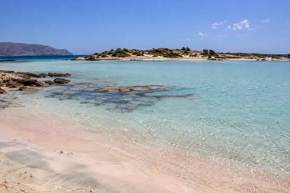 Een ondiepe turquoise lagune, kale eilandjes voor de kust, kale grijze bergen op de achtergrond.