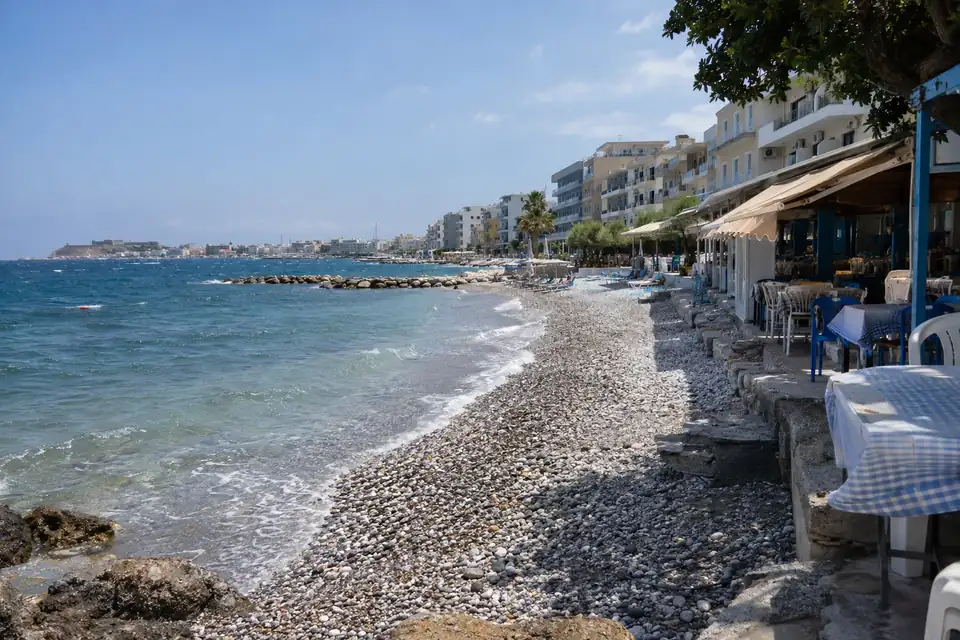 Een strand van grijze en witte kiezels, een beschutte baai, een rij vakantiehotels langs de kustweg.