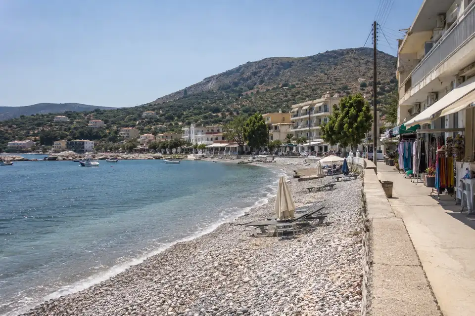 Een strand van grijze en witte kiezels, een beschutte baai, een rij vakantiehotels langs de kustweg.